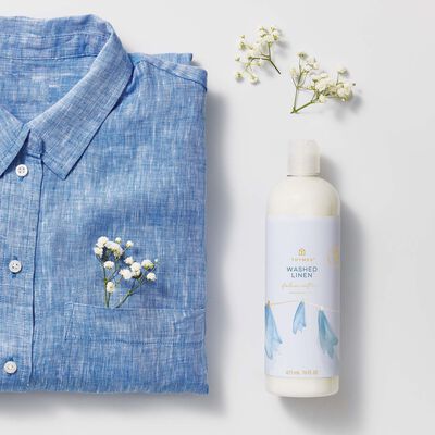 Thymes Washed Linen Fabric Softener for Soft Fabric next to blue shirt and baby's breath flower